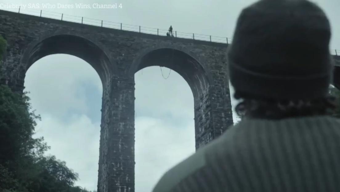 Person watching someone abseil from a bridge.