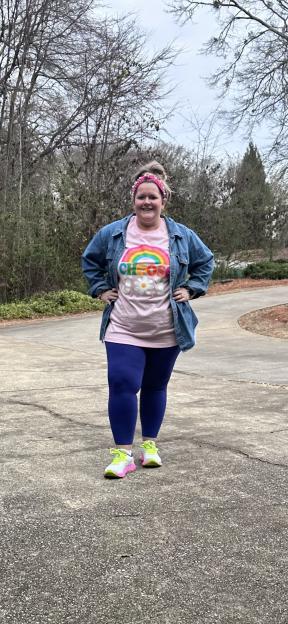 Woman wearing a "Choose Joy" shirt and denim jacket, standing outdoors.