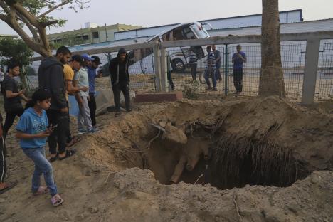 People looking at a large hole in the ground near a damaged bus.