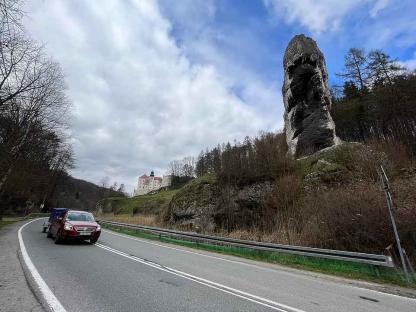 A car drives past a large rock formation and a castle in the background.