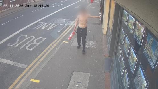 Surveillance image of a shirtless man carrying a fire extinguisher.
