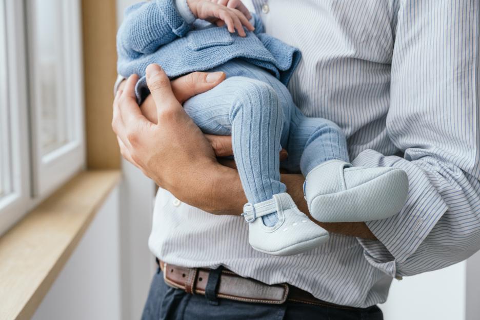 Father embracing a baby boy dressed in blue clothing.