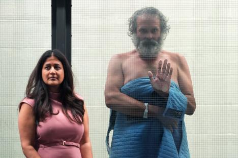 A man and a woman stand behind a wire mesh partition.