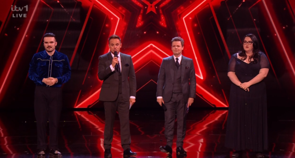 Screenshot of four people on a stage with a red background.