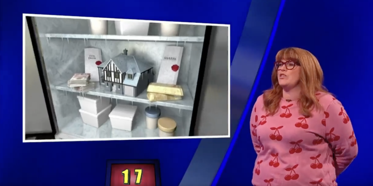 Screenshot of a game show contestant standing next to an image of a shelf containing a house model, gold bars, and documents.