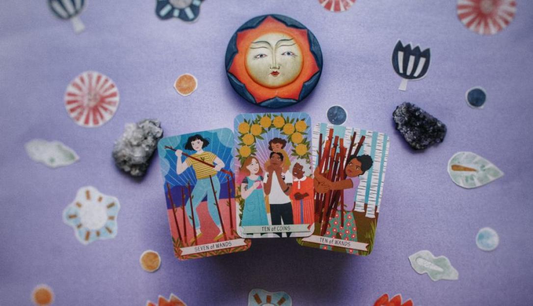 Three tarot cards, Seven of Wands, Ten of Coins, and Ten of Wands, arranged on a purple surface with crystals and decorative elements.