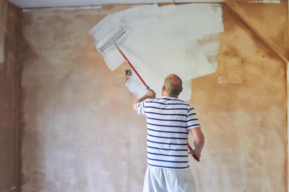 Man painting a wall with a paint roller.