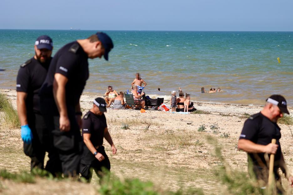 Police officers searching a beach where a murder occurred.