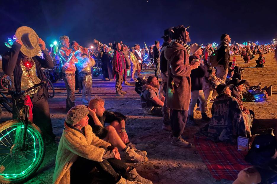 Crowd at Burning Man watching a burning art installation.