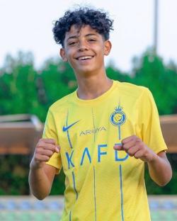 Cristiano Ronaldo's son, Cristiano Jr., smiling and wearing a yellow soccer jersey.