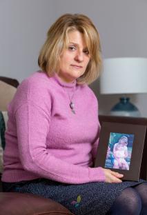 A grieving mother holds a photo of her young daughter.