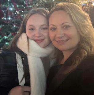 A teenage girl and her mother pose for a selfie in front of a Christmas tree.