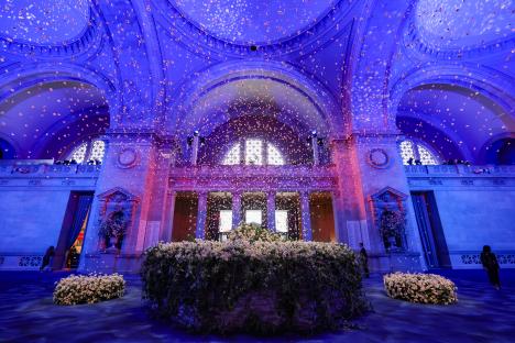 Interior view of the Met Gala venue with flower petals falling from the ceiling and floral arrangements.