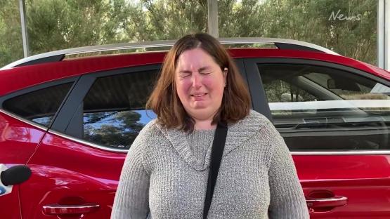 Woman crying in front of a red car.