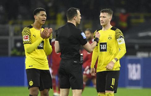 a referee shakes hands with two soccer players wearing yellow jerseys that say 1 & 1