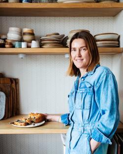Woman in denim overalls holding a plate of sliced blueberry cake.