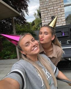 Two blonde women wearing party hats take a selfie.