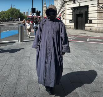 Person in a long robe and face covering walking down a city street.