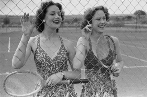 Two young women holding tennis rackets at a holiday camp.