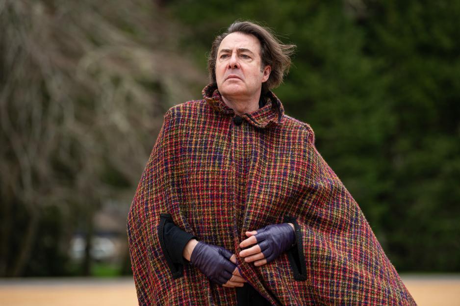 A man wearing a colorful checkered cape and fingerless purple gloves.