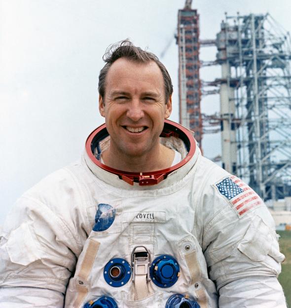 Portrait of Jim Lovell, Apollo 13 commander, in a spacesuit holding a moon globe.