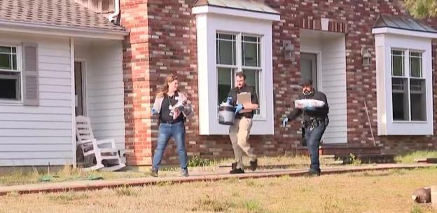 Investigators removing bags and a bucket from a house.