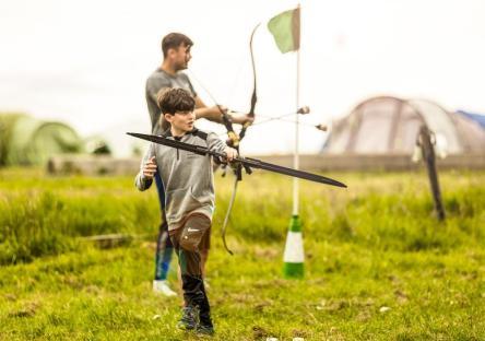 Boy practicing archery with an adult in the background.
