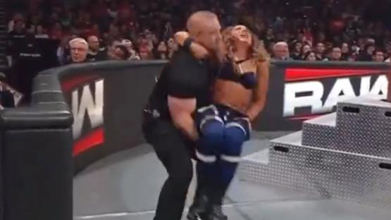 A large man carrying a woman in a wrestling ring.