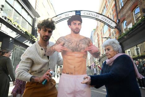 Two people spraying deodorant on a cardboard cutout of a shirtless tattooed man on Carnaby Street.
