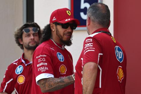 Lewis Hamilton in Ferrari attire speaking with a teammate.