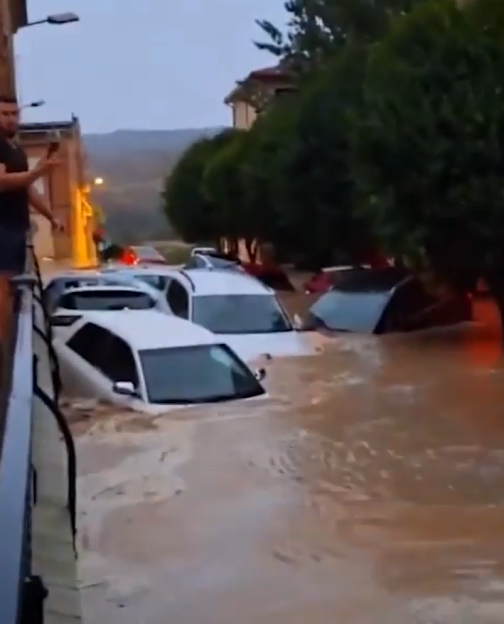 Flooded street with cars submerged in muddy water.