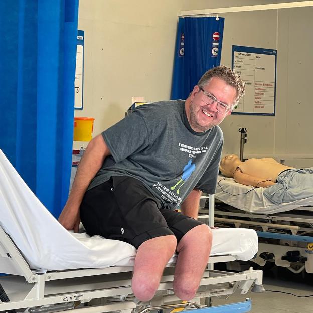 Smiling man with prosthetic legs sitting on a hospital bed.