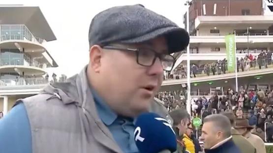 Man in a flat cap being interviewed at a racetrack.