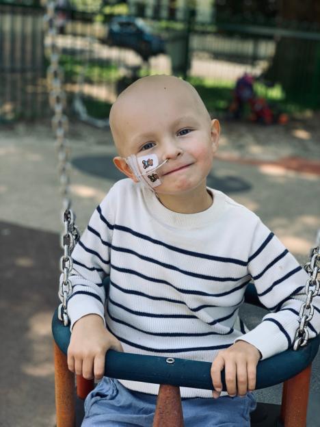 Gaspard Ronsseray, a young boy with cancer, in a swing with a feeding tube taped to his cheek.