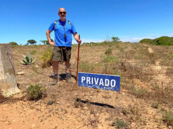 Man standing by a "privado" sign in a dry field.