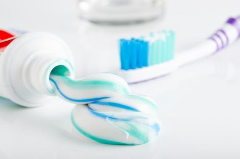 Toothpaste squeezed from a tube onto a white surface, next to a toothbrush and a glass.