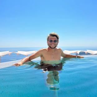 Man in sunglasses relaxing in infinity pool overlooking ocean.
