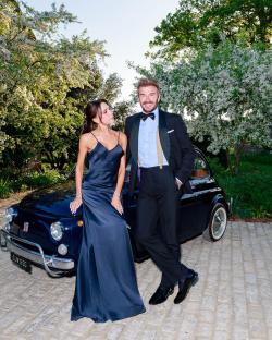 Victoria and David Beckham posing by a classic car.