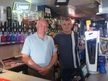 Two men standing behind a pub bar.