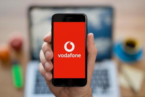 A hand holding an iPhone displaying the Vodafone logo.