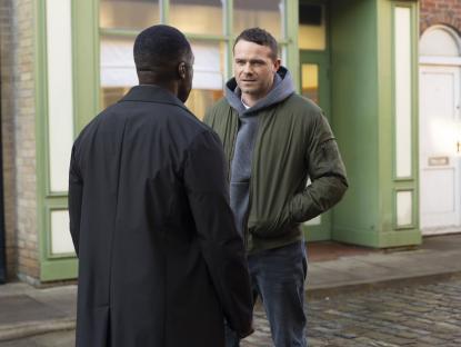 Two men talking on a cobblestone street.