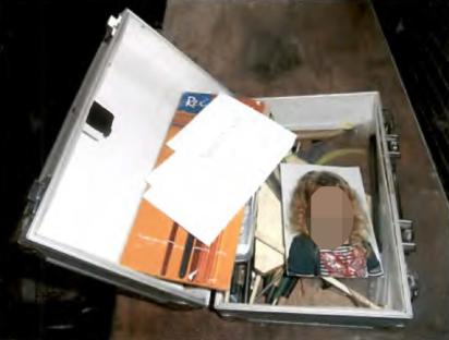 Suitcase containing papers, a drawing, and a photo of a child with its face blurred.