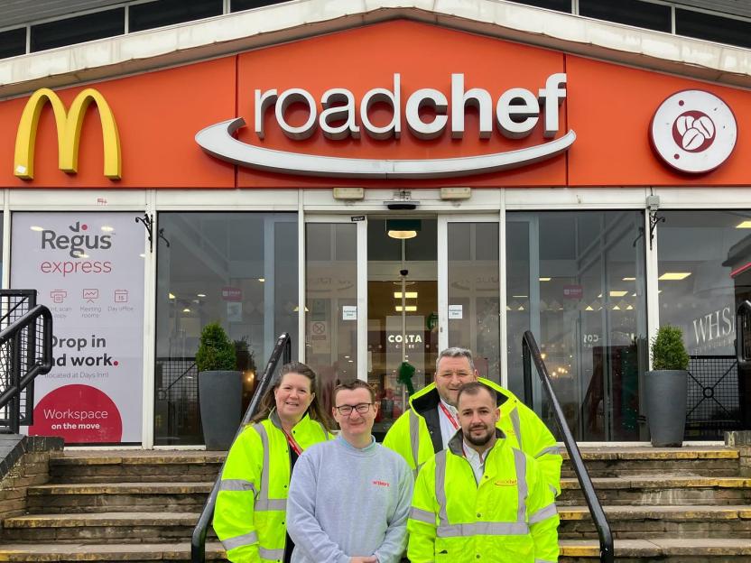 Four people in front of a Roadchef service station with a McDonald's sign and a Regus Express sign visible.