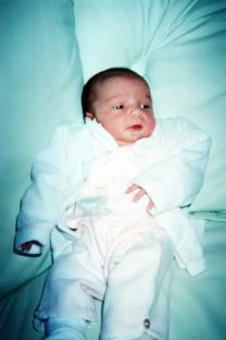 Baby girl in white outfit lying on a light teal surface.