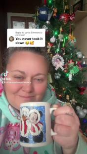 Woman holding a Disney Christmas mug in front of a decorated Christmas tree.