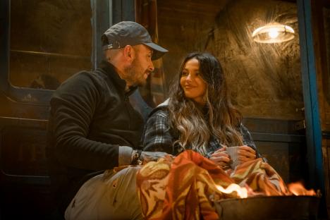 Michelle Keegan and a man sitting close together by a fire, wrapped in a blanket.
