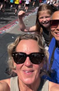 Selfie of a woman with a girl and a man in the background, watching a marathon.