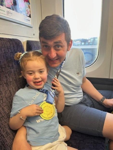 Young girl with her father on a train, she is holding a medal.