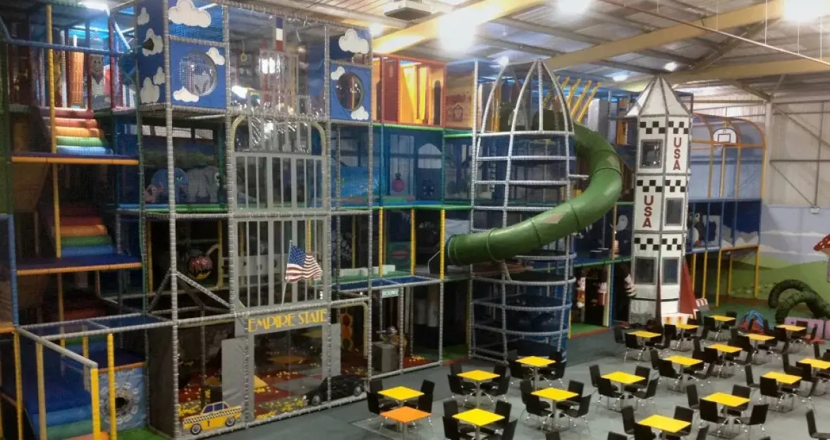 Indoor playground with slides and play structures, alongside tables and chairs for dining.