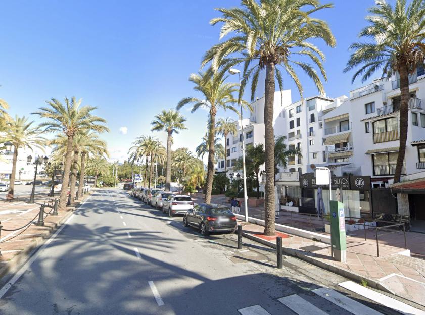Scene of the shooting in Puerto Banus, with palm trees lining a road with parked cars and white buildings.